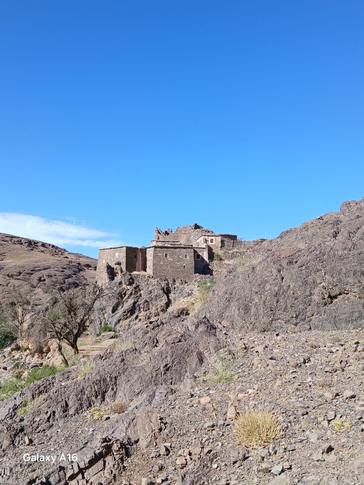 A stone village built along a rocky spur in the Anti-Atlas, its flat-roofed houses following the ridge above bare hillside under a clear blue sky