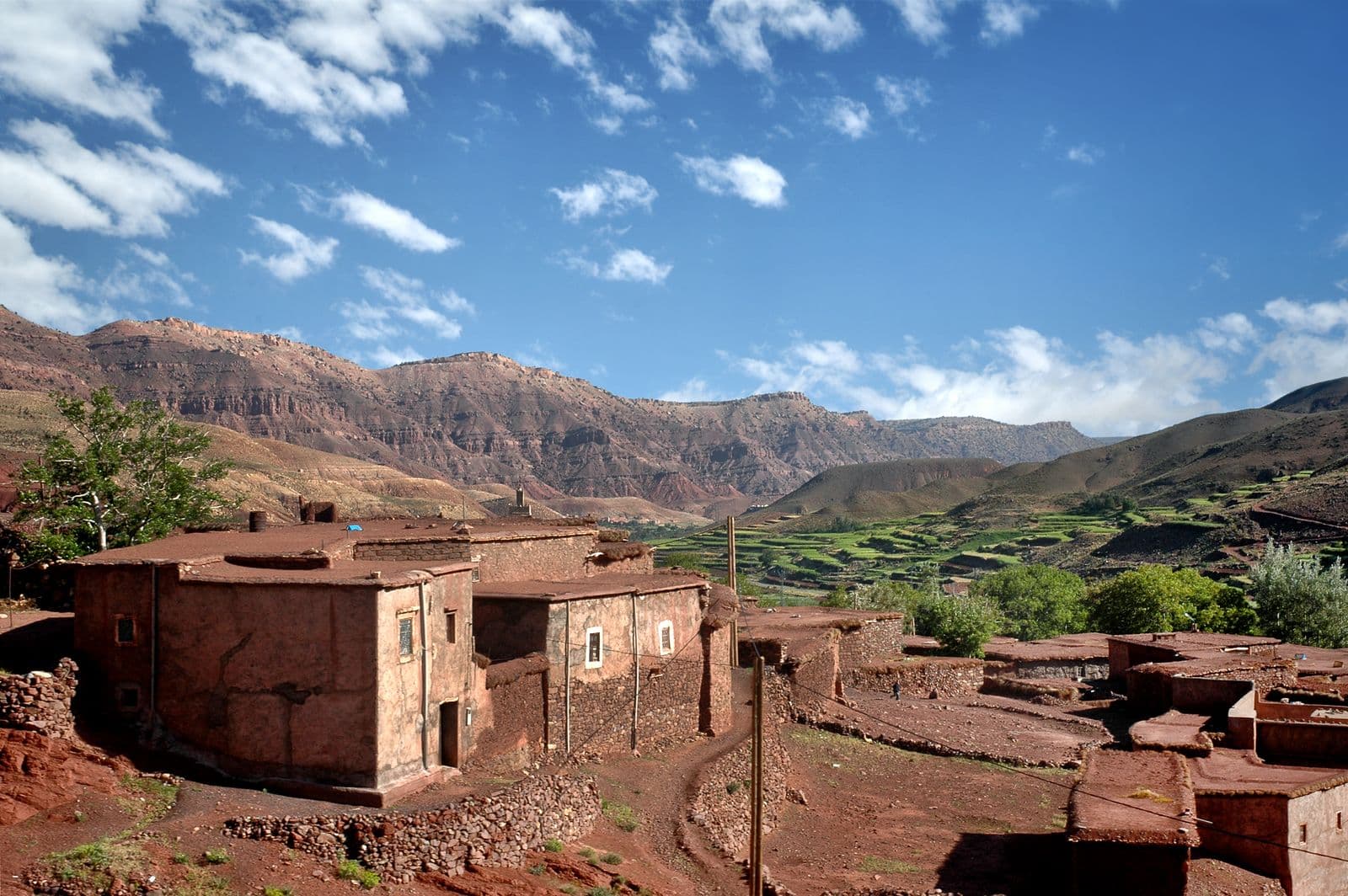 Earthen adobe houses in Ouarzazate stacked against a mountain backdrop under a blue sky with scattered cloud